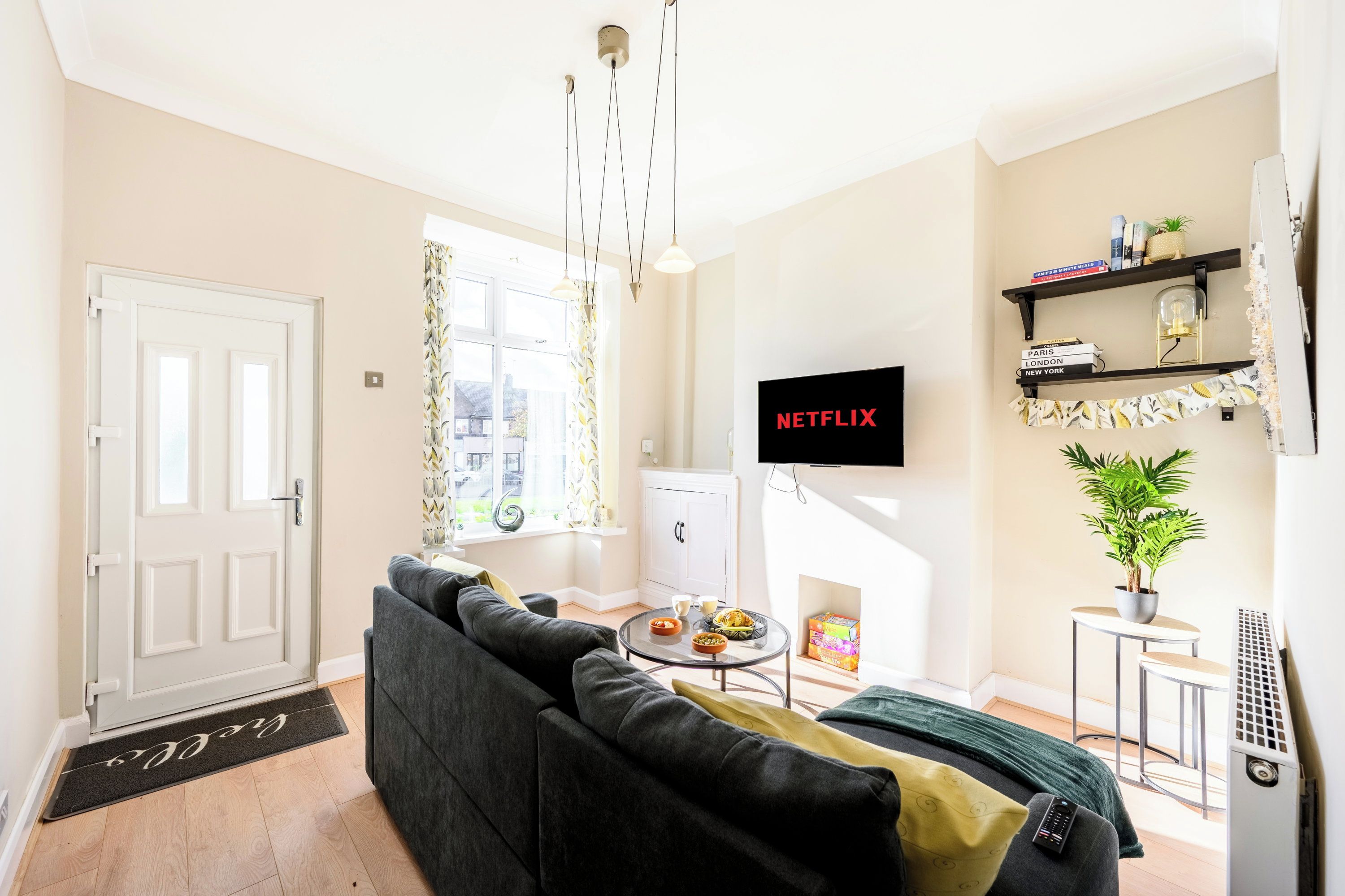 Ein Wohnzimmer mit einer Couch, einem Couchtisch, einem an der Wand befestigten Fernseher und einem Bücherregal.