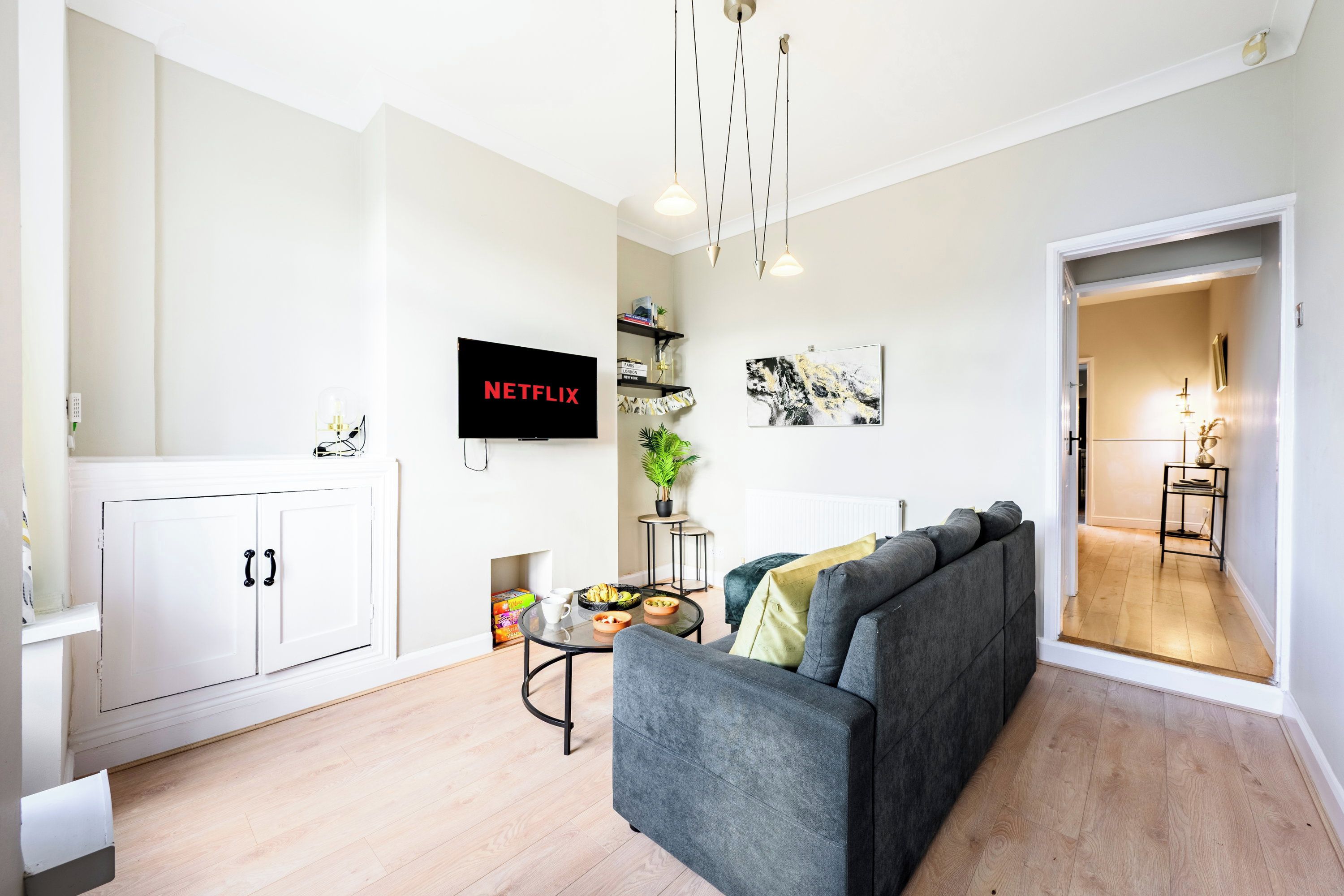A modern living room with a grey sofa, a flat-screen TV, a coffee table, and a bookshelf.