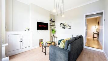 A modern living room with a grey sofa, a flat-screen TV, a coffee table, and a bookshelf.