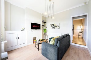 A modern living room with a grey sofa, a flat-screen TV, a coffee table, and a bookshelf. - Renovated, 2 Baths, 2 Lounges, Parking & Garden (Oldbury)