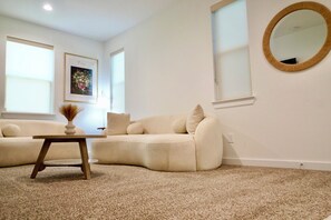 Ein Wohnzimmer mit einem beigefarbenen Sofa, einem kleinen Holztisch und einem runden Spiegel an der Wand.
