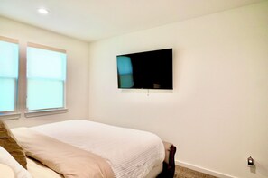 Ein Schlafzimmer mit einem Bett, einem flachbildfernseher an der Wand und einem Fenster mit Jalousien.