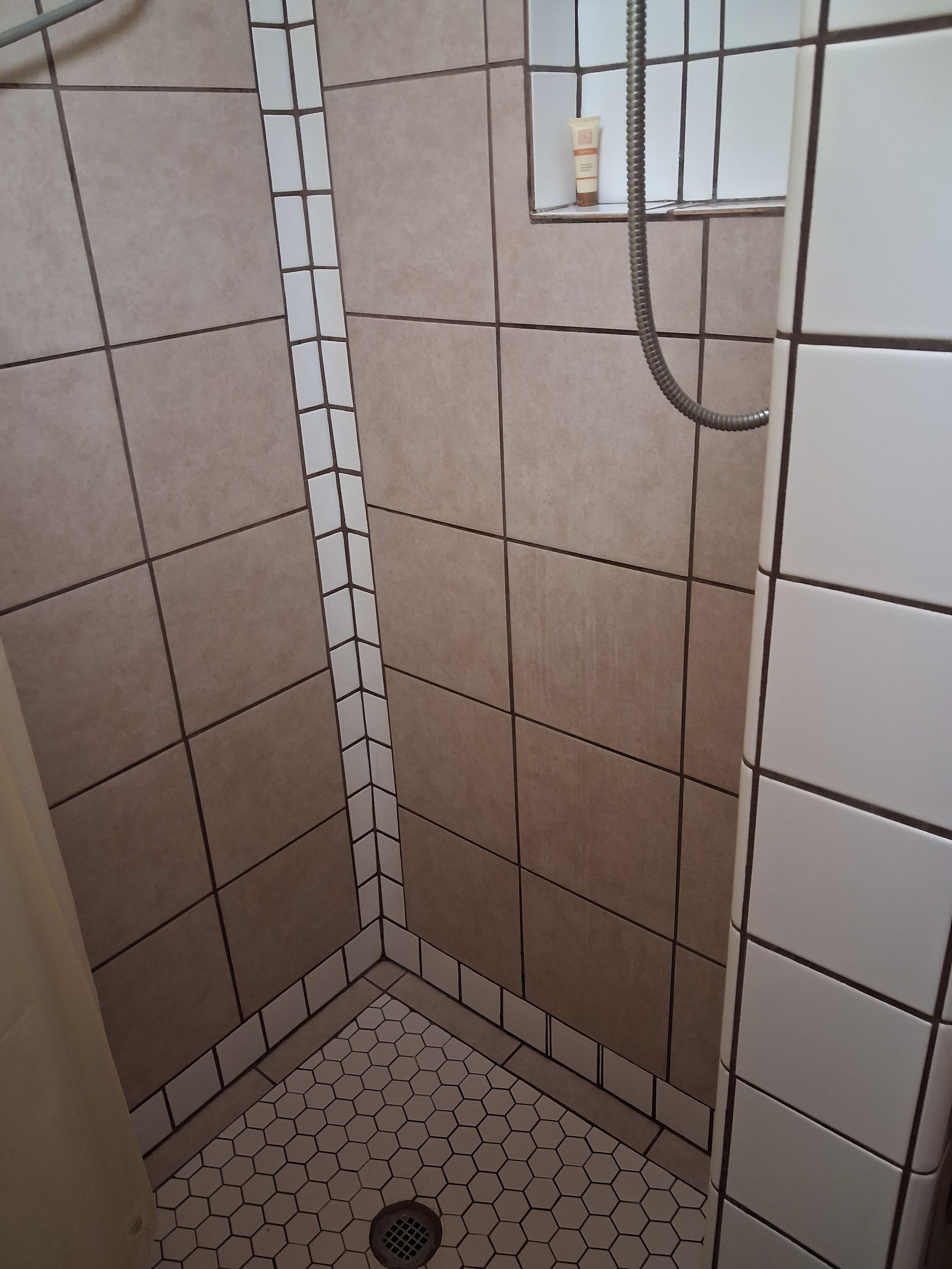 Un área de ducha pequeña, con azulejos, un desagüe y una manguera.