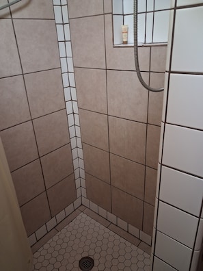 Un área de ducha pequeña, con azulejos, un desagüe y una manguera.