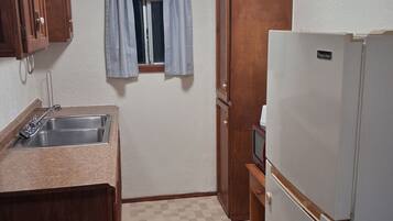 A compact kitchen with a sink, wooden cabinets, a refrigerator, and a window with curtains.