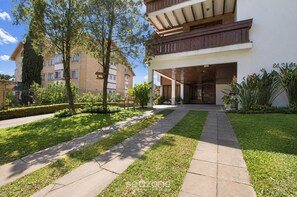 A modern building with a covered entrance, a well-maintained lawn, and a clear sky. - Well-located Apt. w/ BBQ Grill Vcr0206 (Gramado)