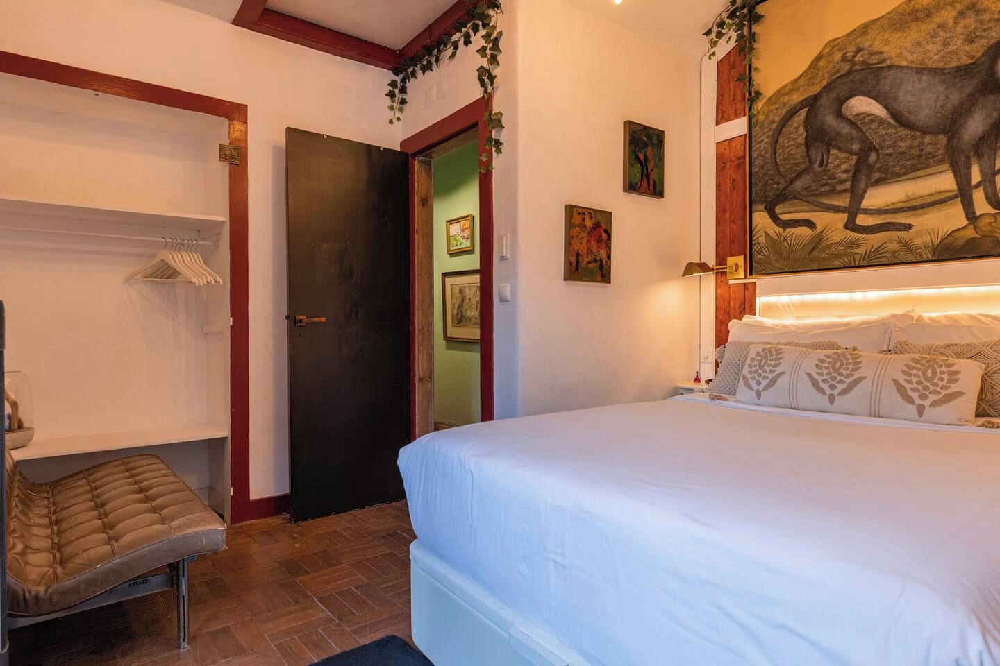 Ein Schlafzimmer mit einem Bett, einem Sessel, einer Tür und Kunstwerken an den Wänden.
