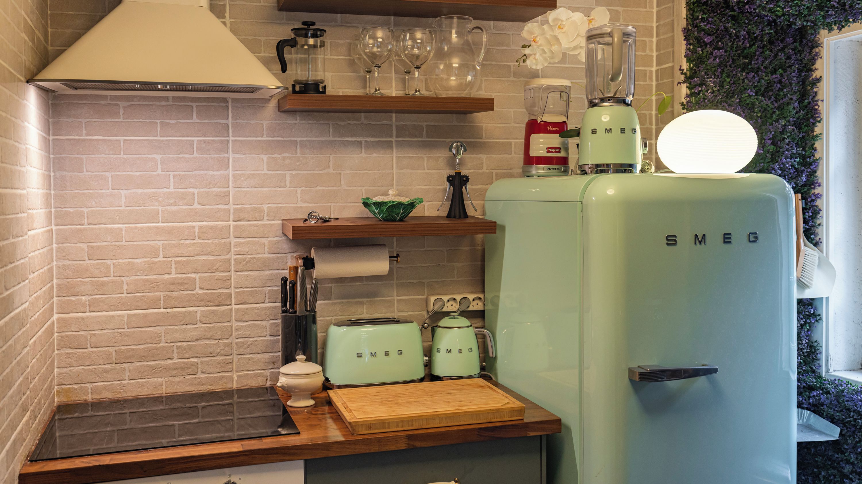 Eine Küche mit Backsteinwand, einem Smeg-Kühlschrank, einer Kaffeemaschine und einer Holzarbeitsplatte.