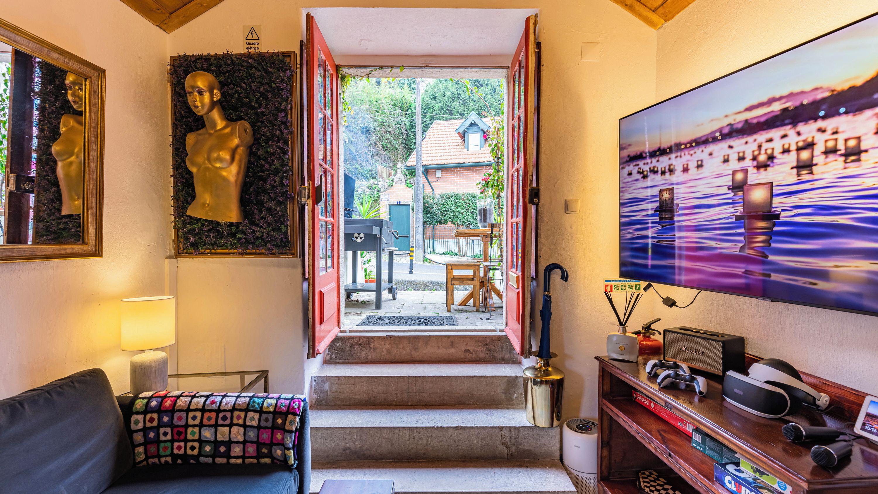A hallway with a staircase leading to a balcony, a television on the wall, and a couch with a colorful cushion.
