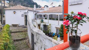 A courtyard with a white building, a red railing, and a potted plant with pink flowers.