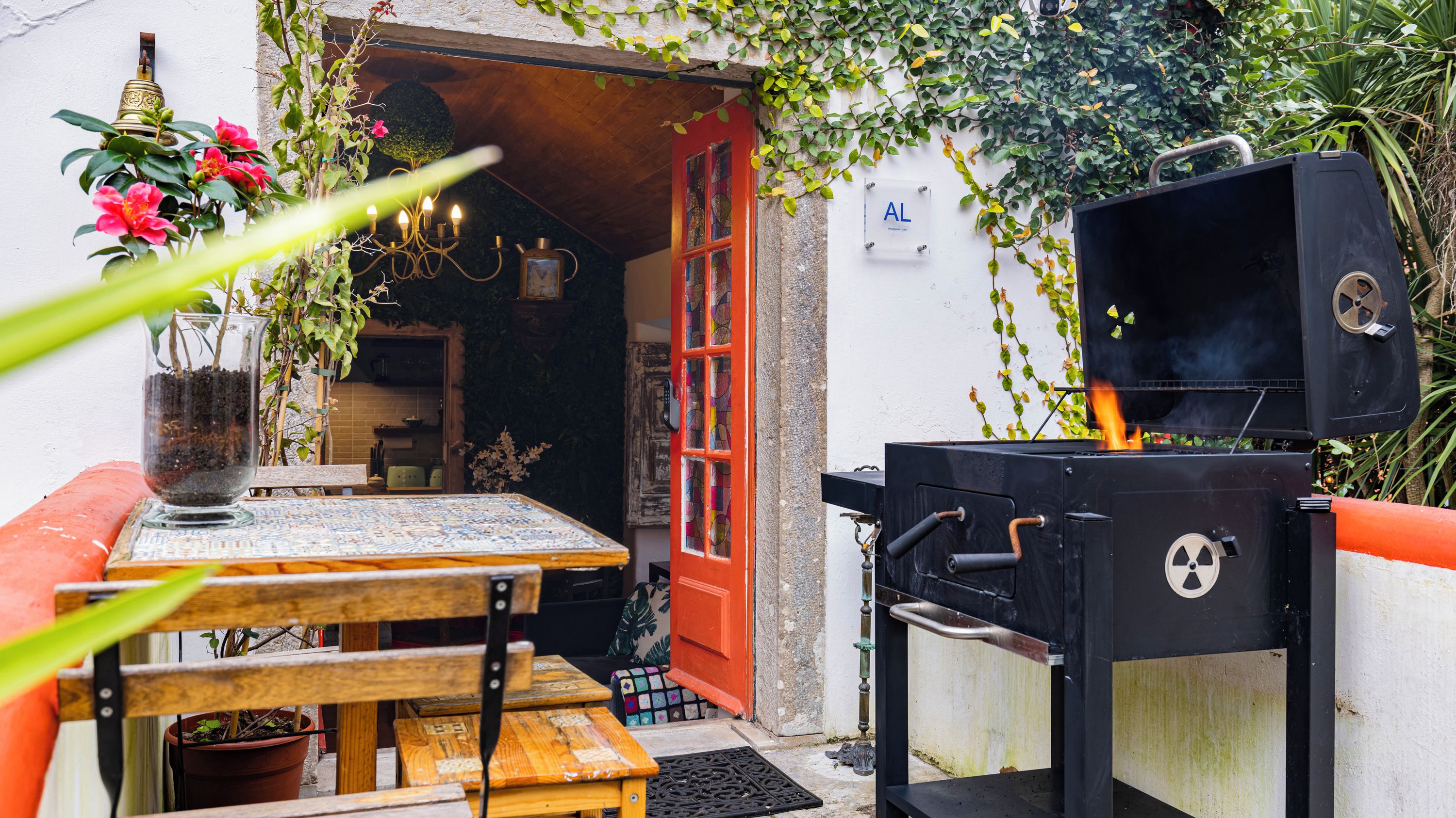Une terrasse extérieure avec une table en bois, un banc, un barbecue et une porte donnant sur un espace cuisine.