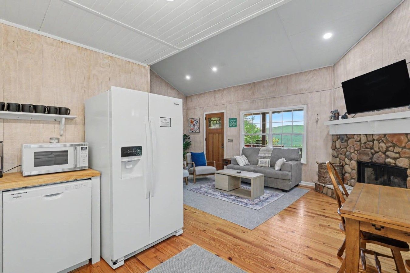 A modern kitchen with a microwave, refrigerator, and dishwasher. There is a seating area with a sofa and a fireplace.