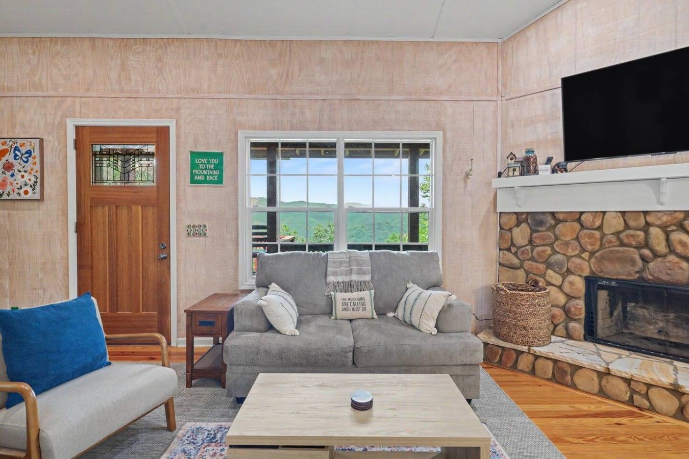 Een gezellige woonkamer met een stenen open haard, een grijze bank, een salontafel en een aan de muur bevestigde televisie.