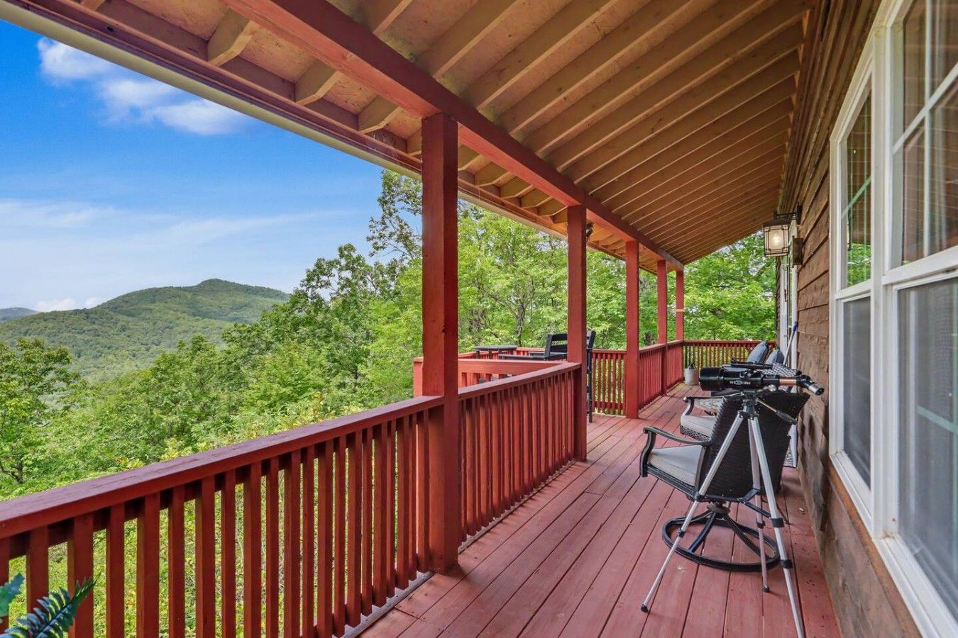 Une véranda couverte avec une terrasse en bois, du mobilier d’extérieur et une vue panoramique sur des collines verdoyantes.