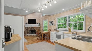 A modern kitchen with a stone fireplace, wooden dining table, and large windows.