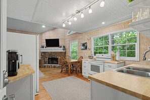 A modern kitchen with a stone fireplace, wooden dining table, and large windows.