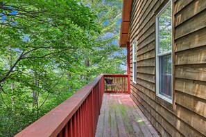 Une terrasse en bois avec une rambarde rouge, entourée d’arbres verdoyants.