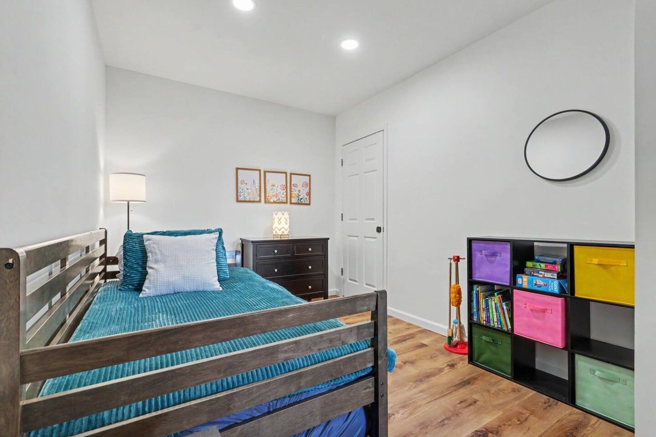 Een slaapkamer met een bed, een kaptafel, een bedlampje, wanddecoratie en een boekenplank.