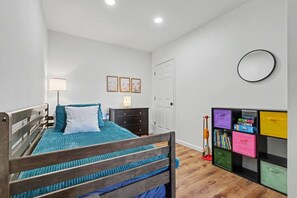 Une chambre à coucher comprenant un lit, une commode, une lampe de chevet, des œuvres d’art murales et une bibliothèque.