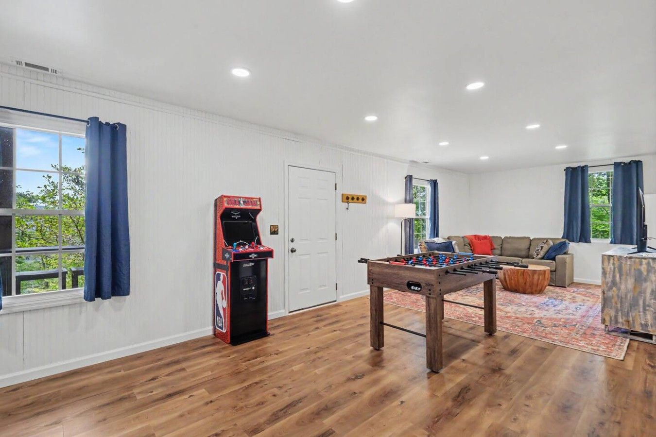 A room with a foosball table, a door, a sofa, and a window with curtains.