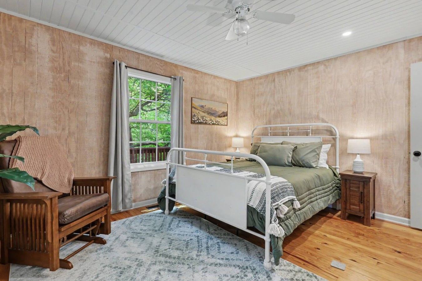 A bedroom with a bed, bedside tables, a chair, a window, and a ceiling fan.