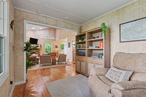 Un salon chaleureux avec un plancher en bois, un canapé, une bibliothèque et un coin repas comprenant des chaises et une table.