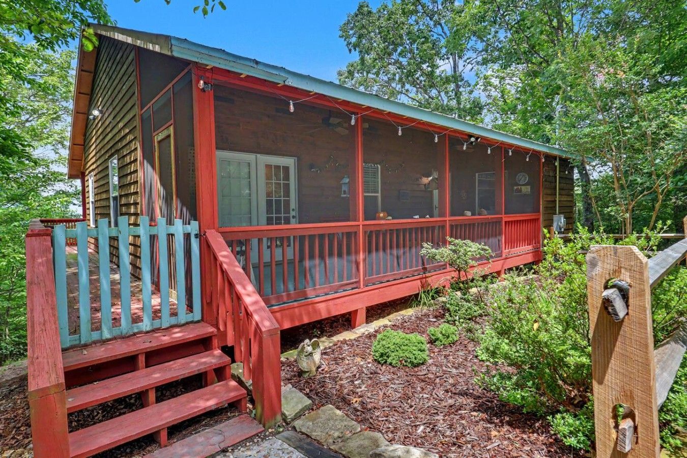 A wooden cabin with a red porch and a blue gate.