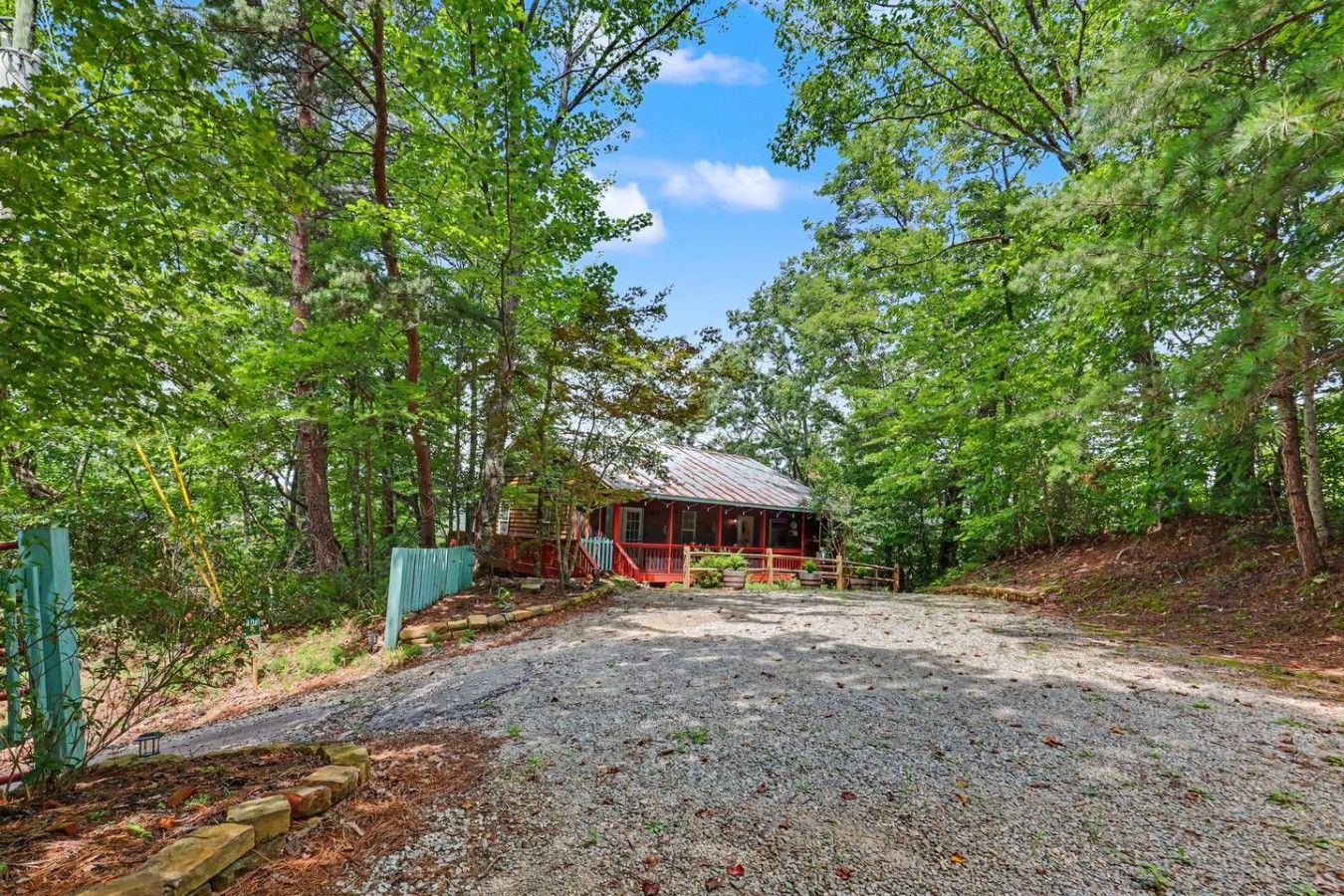A rustic cabin with a gravel driveway leading to a wooden fence.