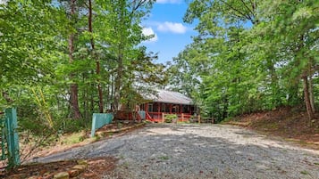 A rustic cabin with a gravel driveway leading to a wooden fence.