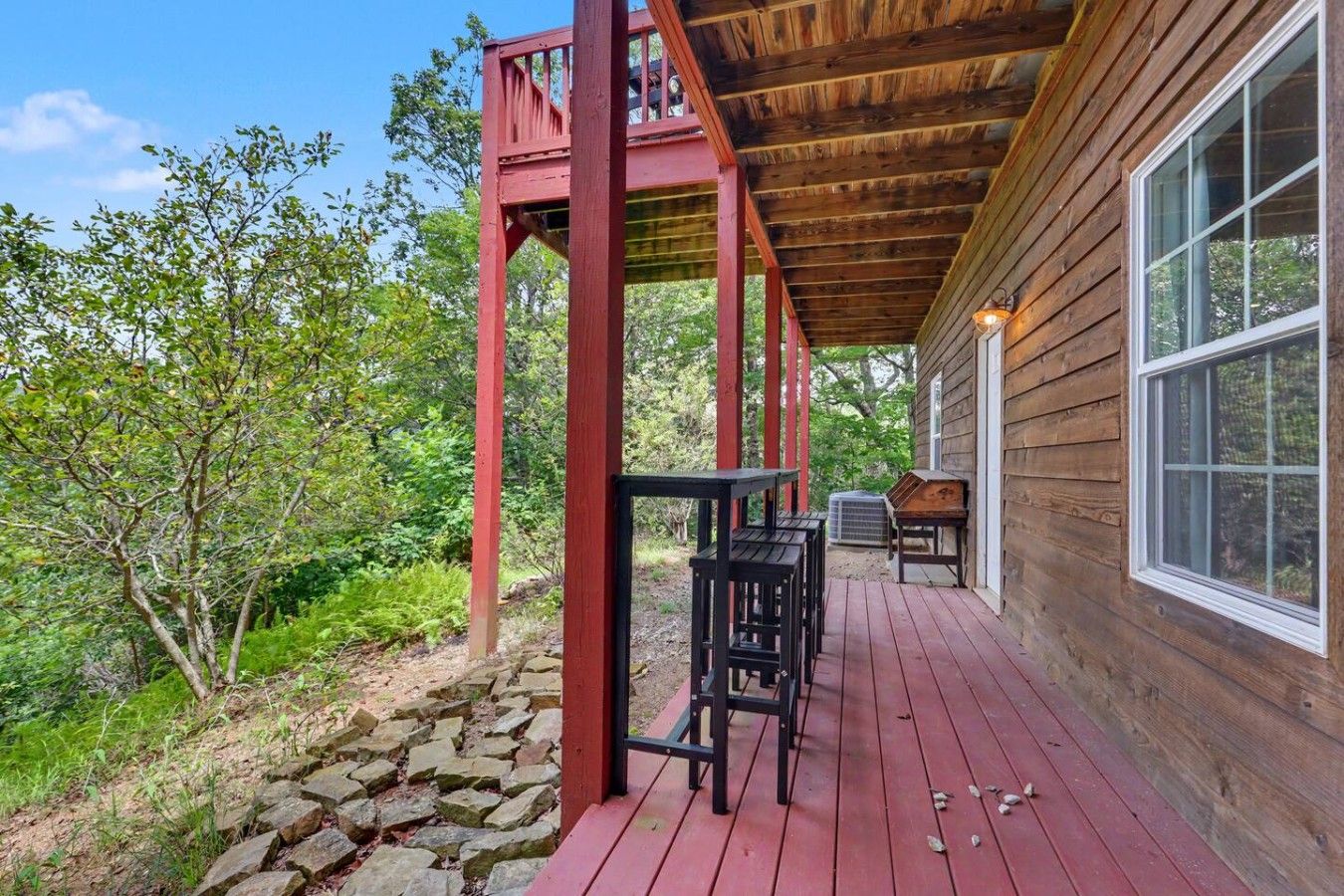 A wooden deck with a red railing, a stone wall, and a view of a forest.