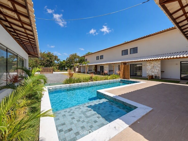 A modern residential property with a swimming pool, a covered patio, and a stone facade.