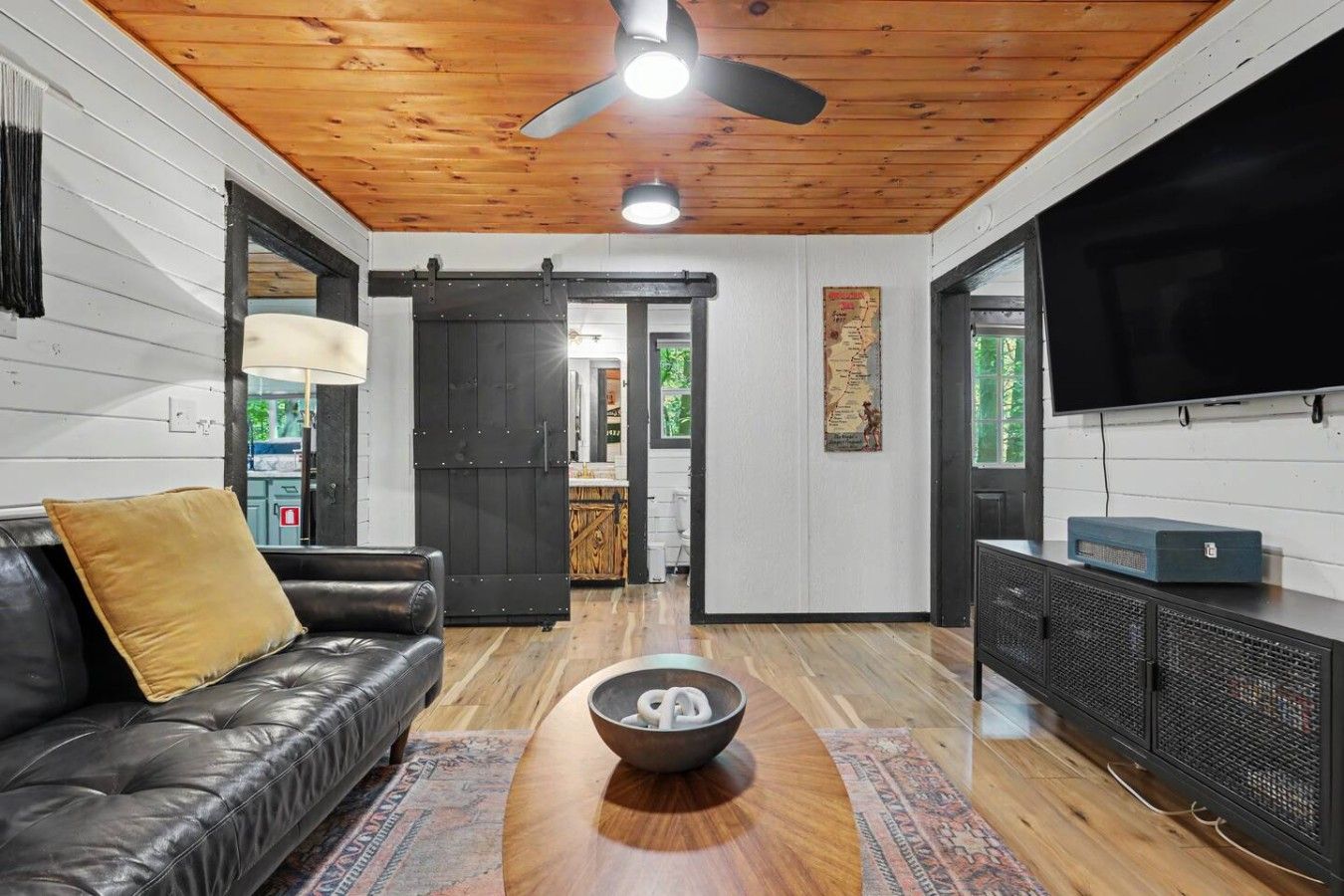 A modern living room with a black leather sofa, a wooden coffee table, a television, and a ceiling fan.