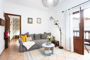 Un salon avec un canapé, une petite table ronde sur laquelle est posé un vase, un lampadaire et une porte donnant sur l’extérieur.