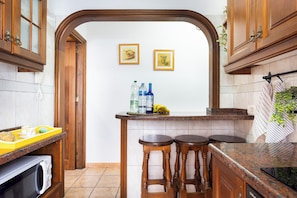 Una cocina con armarios de madera, un microondas, un lavamanos y dos taburetes.