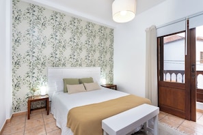 A bedroom with a bed, bedside tables, a bench, a door, and a window. - TenoHomes La Perla Natural Pools Garachico (Garachico)