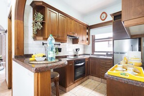 A kitchen with wooden cabinets, a stainless steel refrigerator, and a countertop with a water bottle and bananas. - TenoHomes La Perla Natural Pools Garachico (Garachico)
