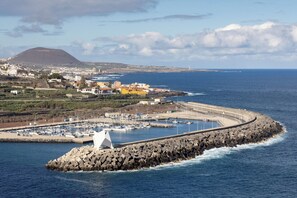 Un pueblo costero con un puerto deportivo, un rompeolas rocoso y una montaña al fondo.