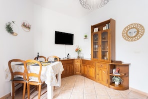 Un coin repas avec une table dressée pour deux personnes, des chaises en bois, un meuble avec des portes en verre et un téléviseur à écran plat fixé au mur.