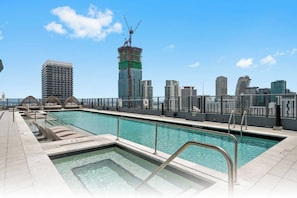Une piscine sur le toit, avec la vue sur les toits de la ville en arrière-plan, dont un immeuble en construction.