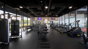 Ett gym med olika typer av träningsutrustning, stora fönster och en central gång.
