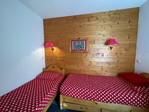 Een kamer met twee houten bedden, elk voorzien van een rood-wit gebedde en twee wandlampen met rode kapjes.