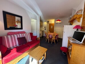 Ein kompakter Wohnbereich mit einem roten Sofa, einem Holztisch und einem Essbereich inklusive Tisch und Stühlen.