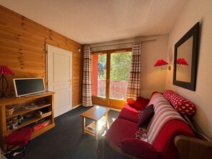 Ein gemütliches Zimmer mit Holzeinrichtung, einem roten Sofa, einem kleinen Tisch und einem Fernseher auf einem Holzständer.