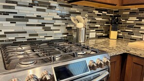 Cozinha equipada com fogão a gás, eletrodomésticos de aço inoxidável e painel decorativo com padrão de mosaico.