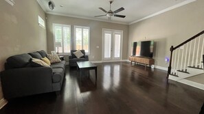 A spacious living room with a dark wood floor, a gray sofa, a coffee table, and a TV stand with a flat-screen TV. - Luxury Sanctuary, North Hyde Park- Private Hot Tub (Tampa)