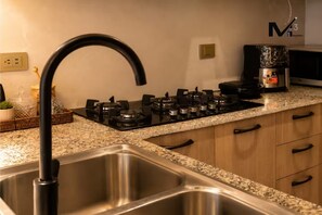 A kitchen with a stainless steel sink, a gas stove with multiple burners, and wooden cabinets. - Luxury Apt / Pool / Steps to BlueMall (Santo Domingo)