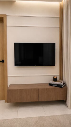 A flat-screen TV mounted on a wall with a wooden console below. - Luxury Apt / Pool / Steps to BlueMall (Santo Domingo)