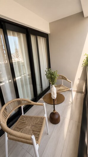 A balcony with two wicker chairs, a round table, and a potted plant. - Luxury Apt / Pool / Steps to BlueMall (Santo Domingo)