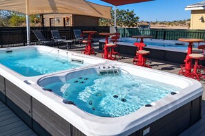 Un espace piscine aménagé sur le toit, comprenant deux bains à remous, des chaises longues et des tables rouges.