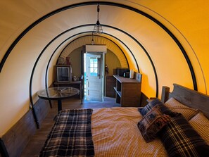 A cozy, circular room with a bed, a small table, and a door leading to another room. - Wagon 5 Cozy 1-bedroom recreational vehicle with AC in terrific Casa Grande (Casa Grande)